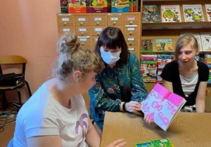 Pracownik Biblioteki Miejskiej w Radomsku czyta dziewczynkom, uczestnikom Programu Rehabilitacja 25 plus książkę podczas wizyty w bibliotece.